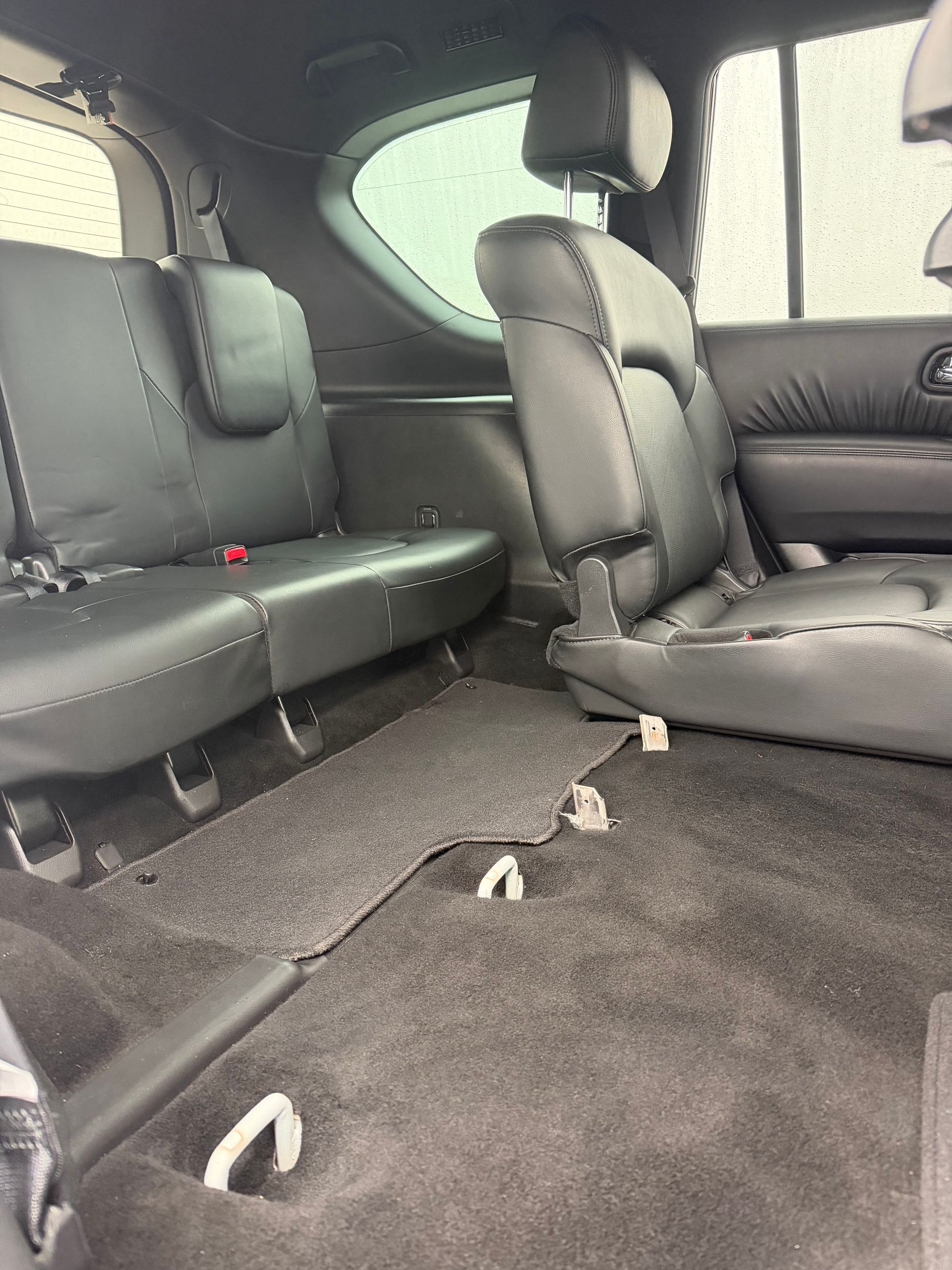Interior of a vehicle with folded black seats and gray carpet, showing a spacious cargo area