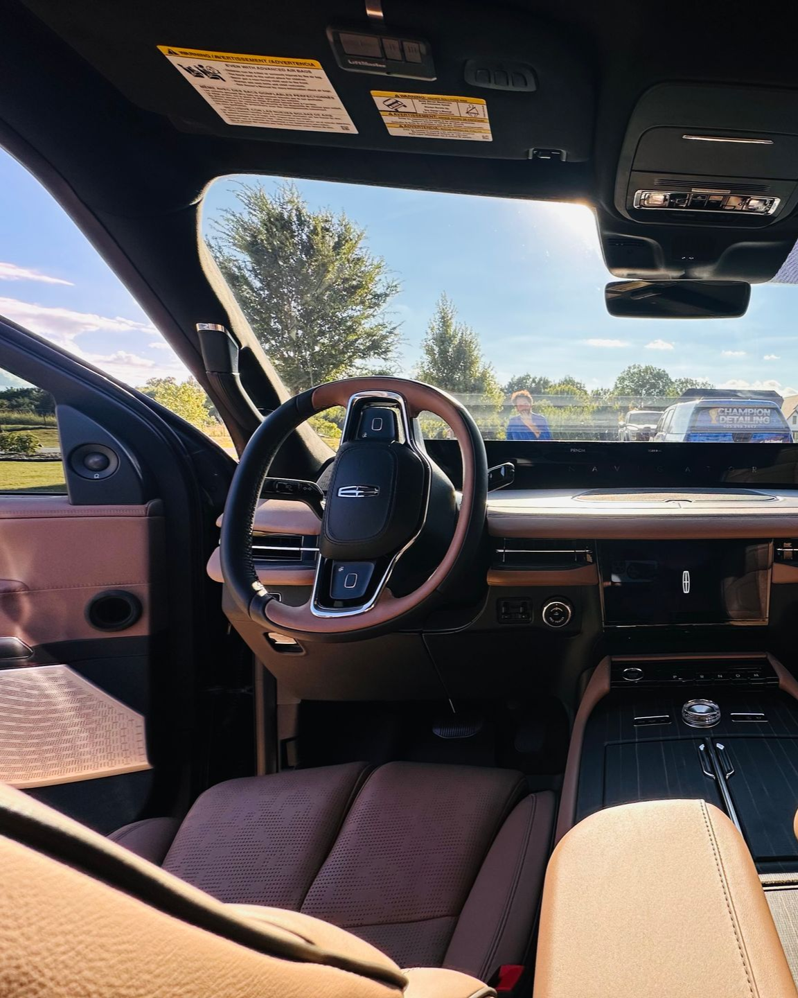 Luxury car interior with tan seats, wood steering wheel, and panoramic sunroof viewed from the driver’s side