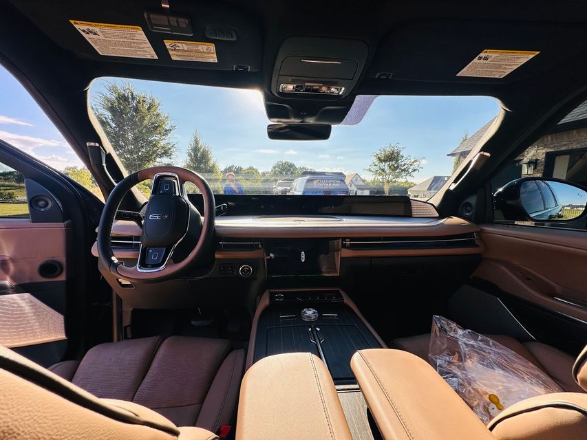 Luxury car interior with tan leather seats, panoramic roof, and dashboard view through the windshield.