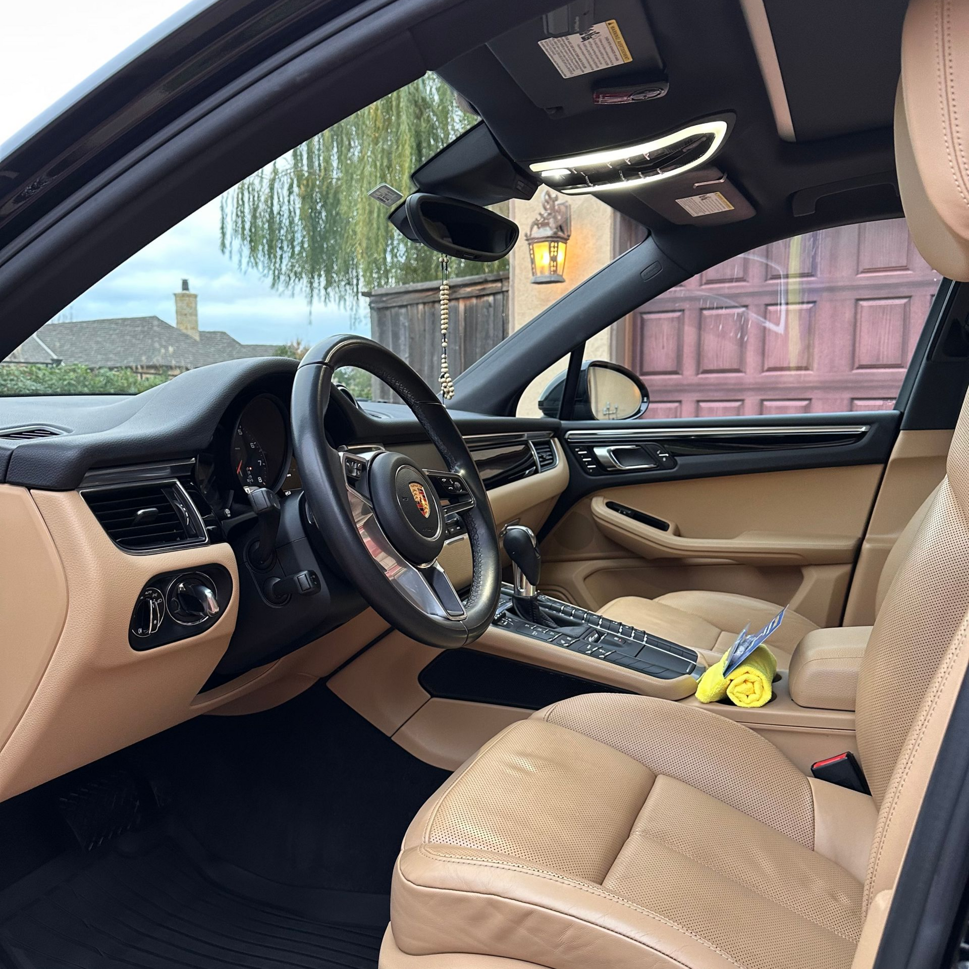 Car interior with tan seats and dashboard, steering wheel, and open door, viewed from the passenger side.
