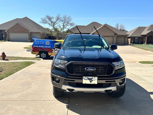 Blue pickup truck parked in a driveway beside a brick house on a sunny day