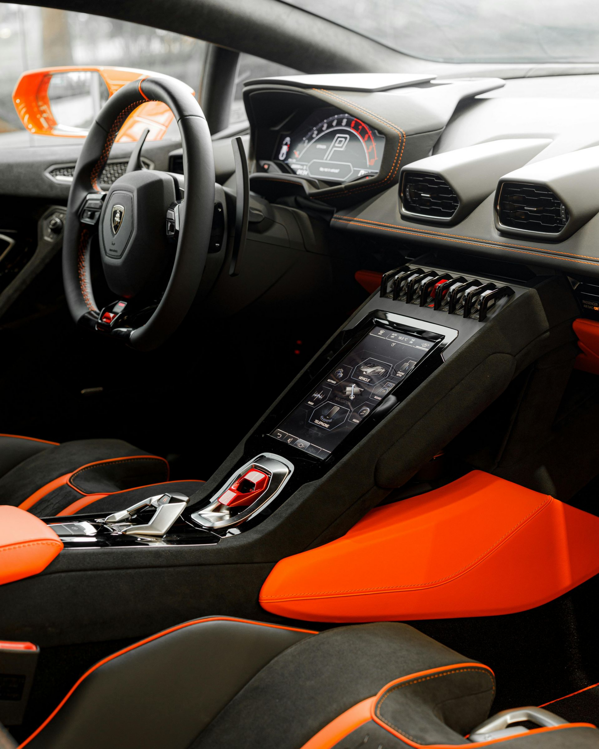 Interior of a sports car with black and orange seats, dashboard, and center console displayed from the driver’s side