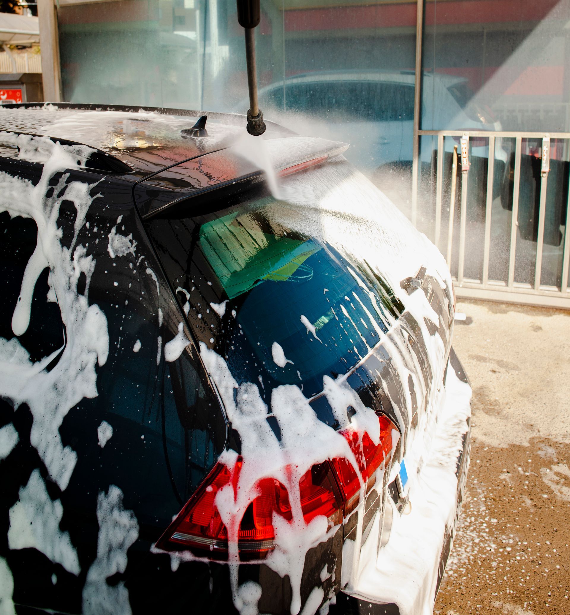 Car being washed with soapy foam, rear window and taillight visible