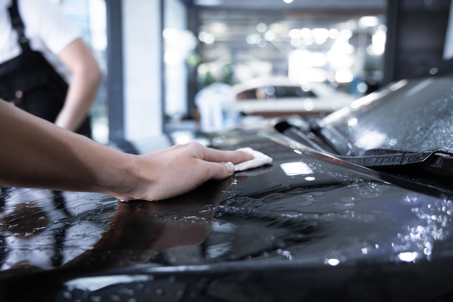 Person wiping a black car with a cloth in an indoor garage.