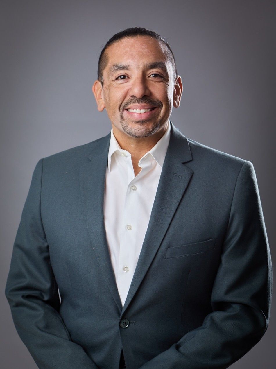 Man in blue suit smiles at the camera; light-colored background.