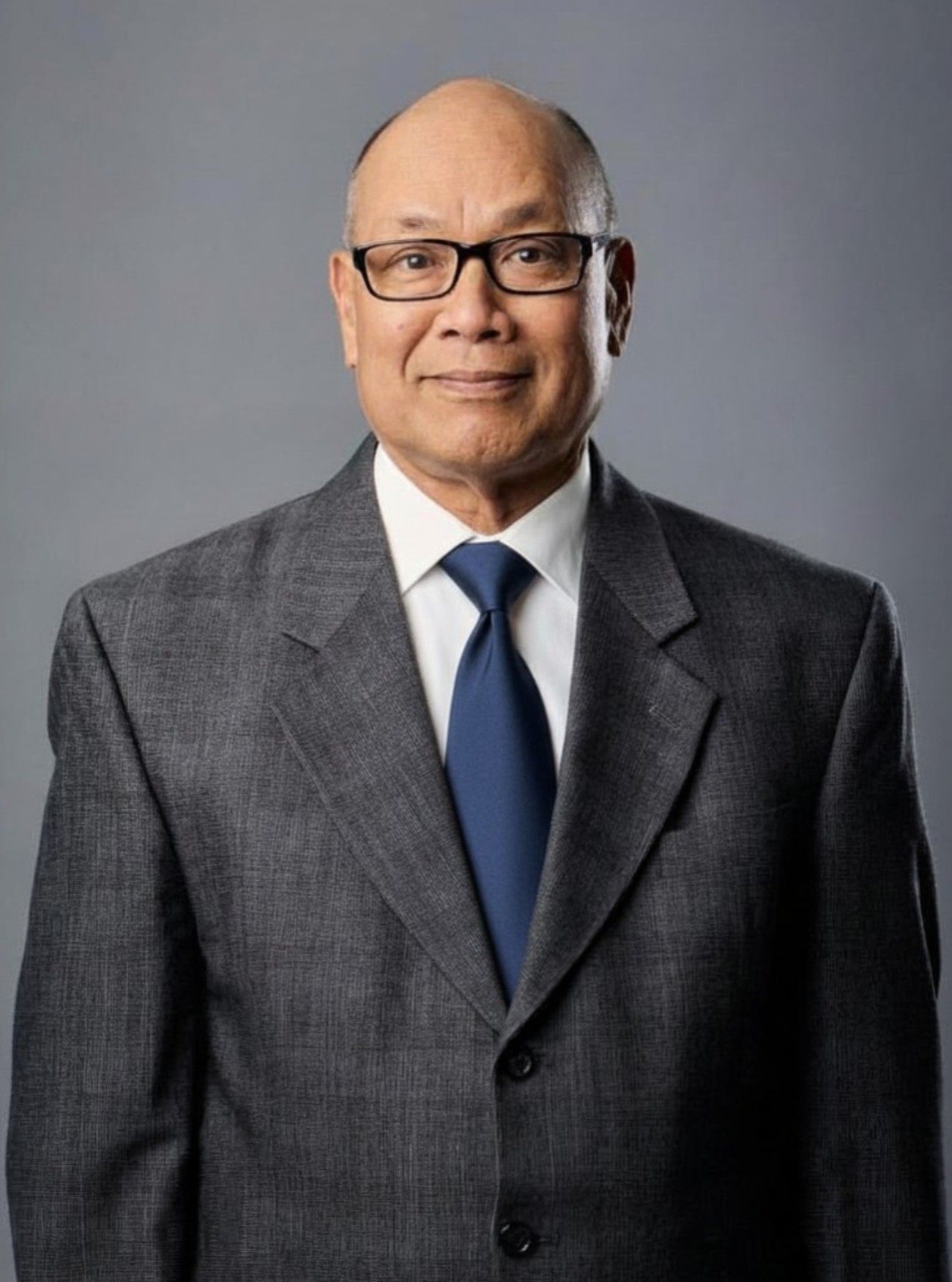 Man in a suit, wearing glasses, smiles. Indoors, near a window.