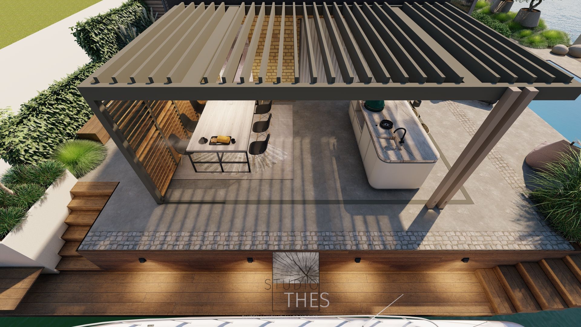Buitenkeuken onder een pergola: eettafel, kookeiland met spoelbak, houten terras en waterpartij.