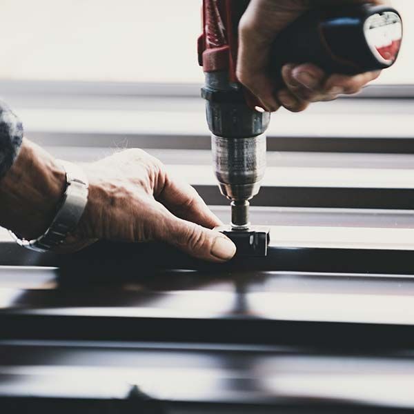 Hands using a power drill to fasten a screw into a black metal surface