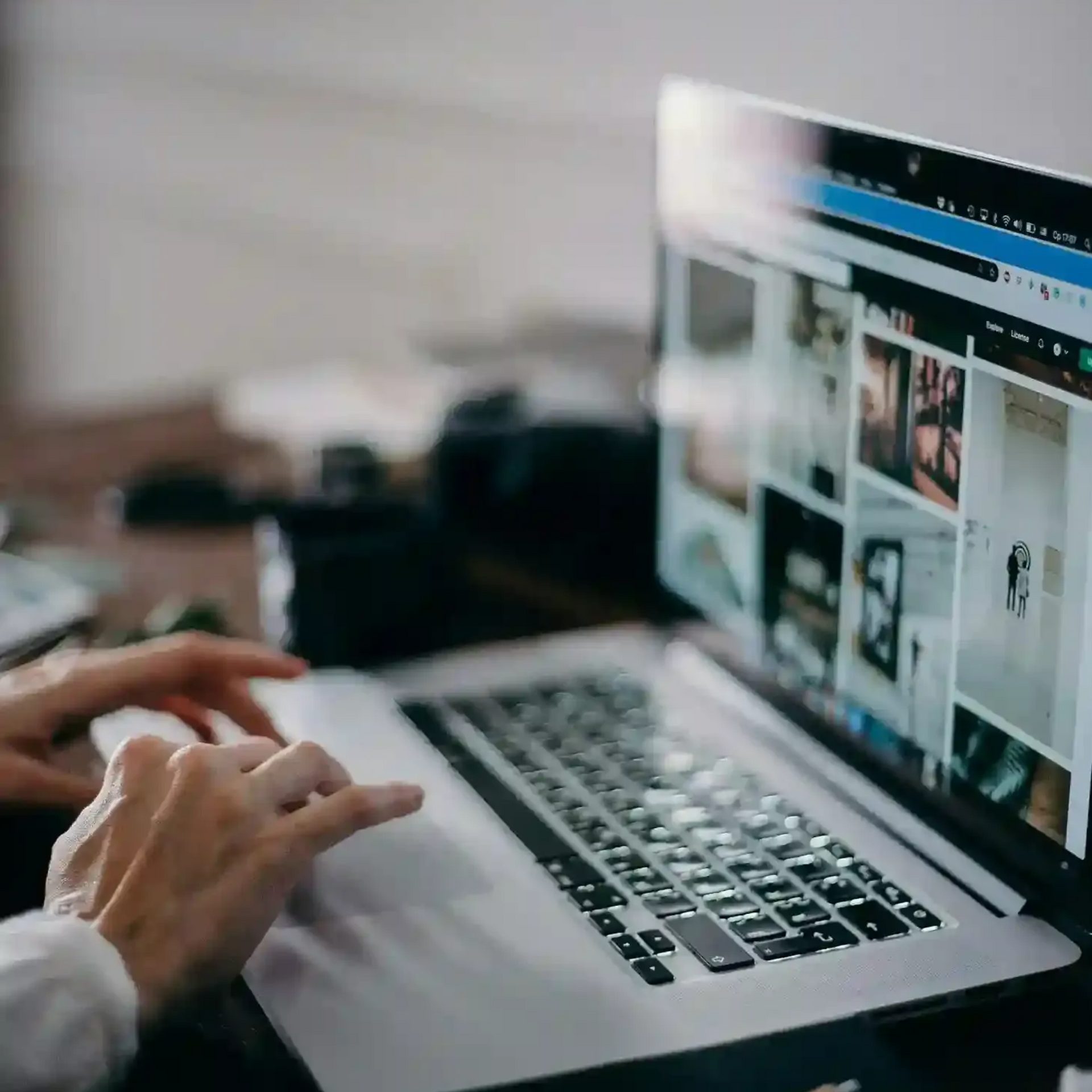 Hands resting on a laptop trackpad and keyboard while viewing a gallery of images on the screen.