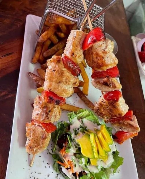 Two skewers of grilled chicken and red peppers served with a wire basket of fries and a side salad