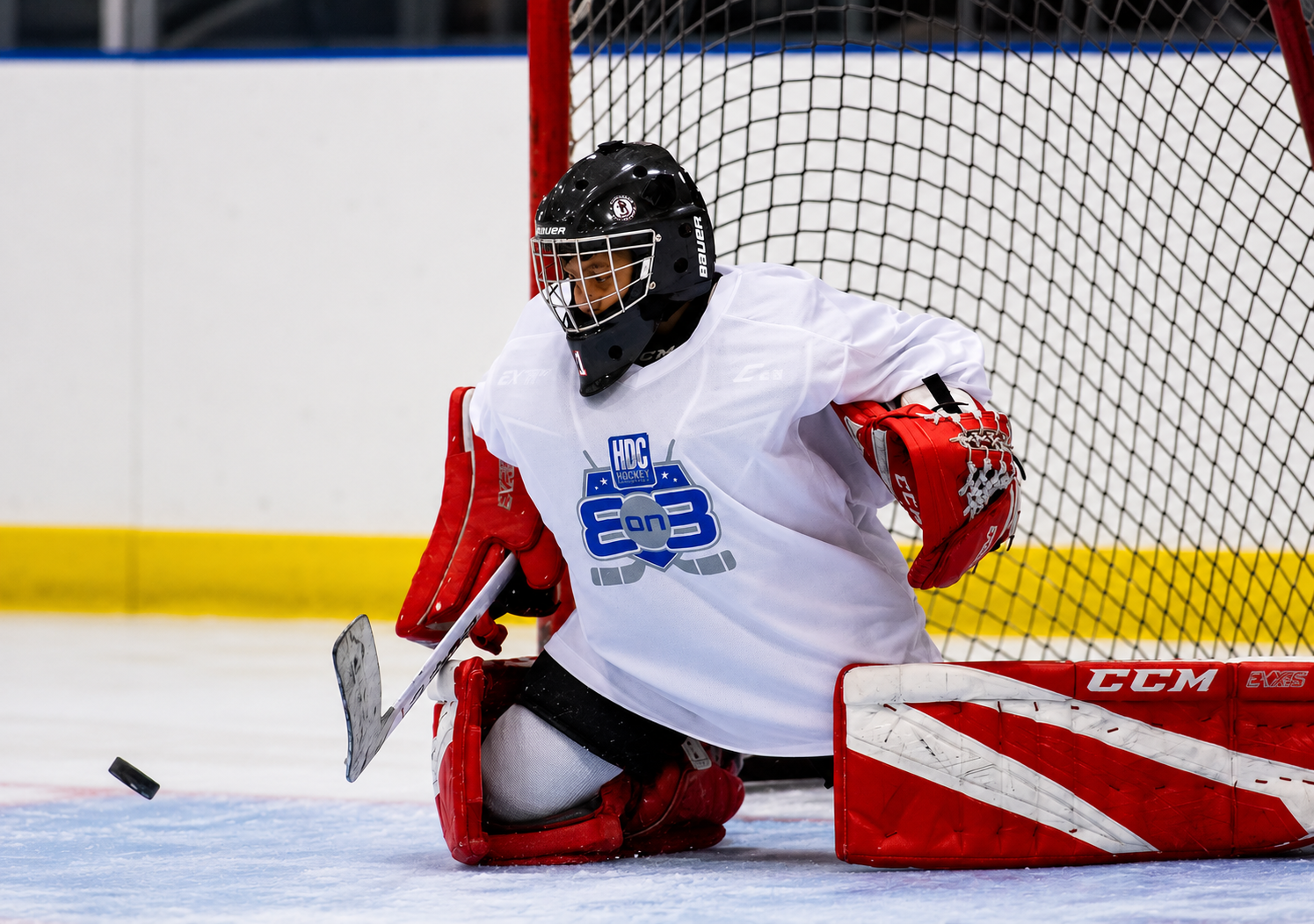 Ice hockey goalie in white and red gear kneeling in front of the net with a puck nearby