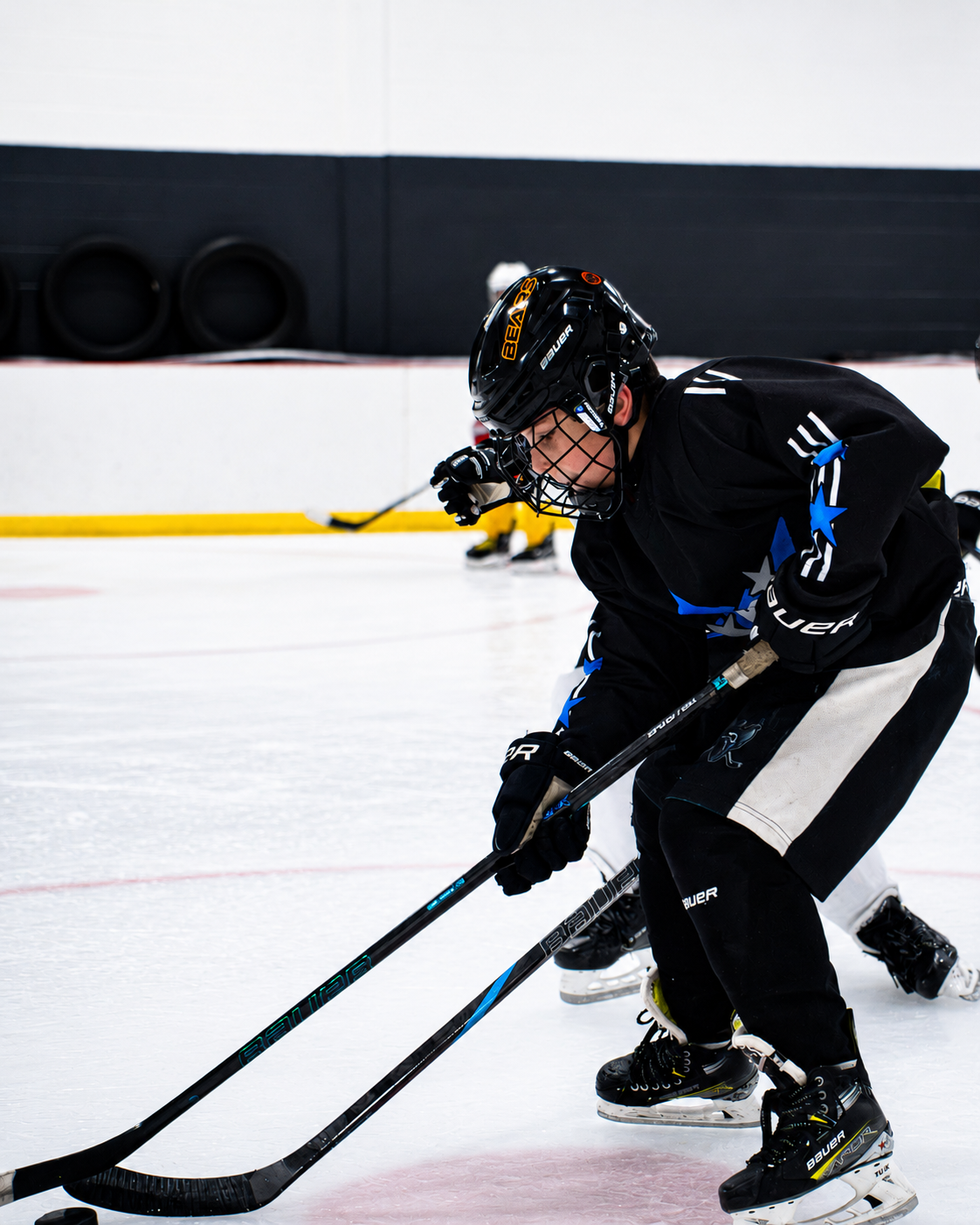 Ice hockey player in black jersey skating and handling the puck on an indoor rink