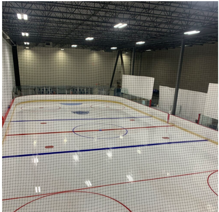 Indoor ice rink viewed from above, with white ice, red and blue lines, and netting in front.