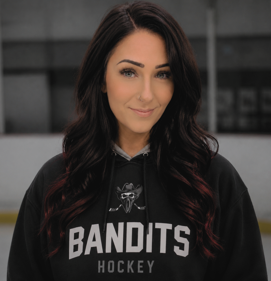 Woman in a black BANDITS hockey hoodie, smiling in front of a blurred indoor background.