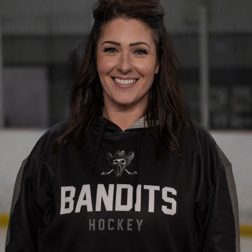 Woman in a black BANDITS hockey hoodie, smiling in front of a blurred indoor background.
