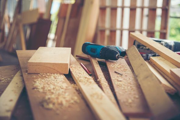 Woodworking bench with lumber, wood shavings, and a cordless drill in a workshop