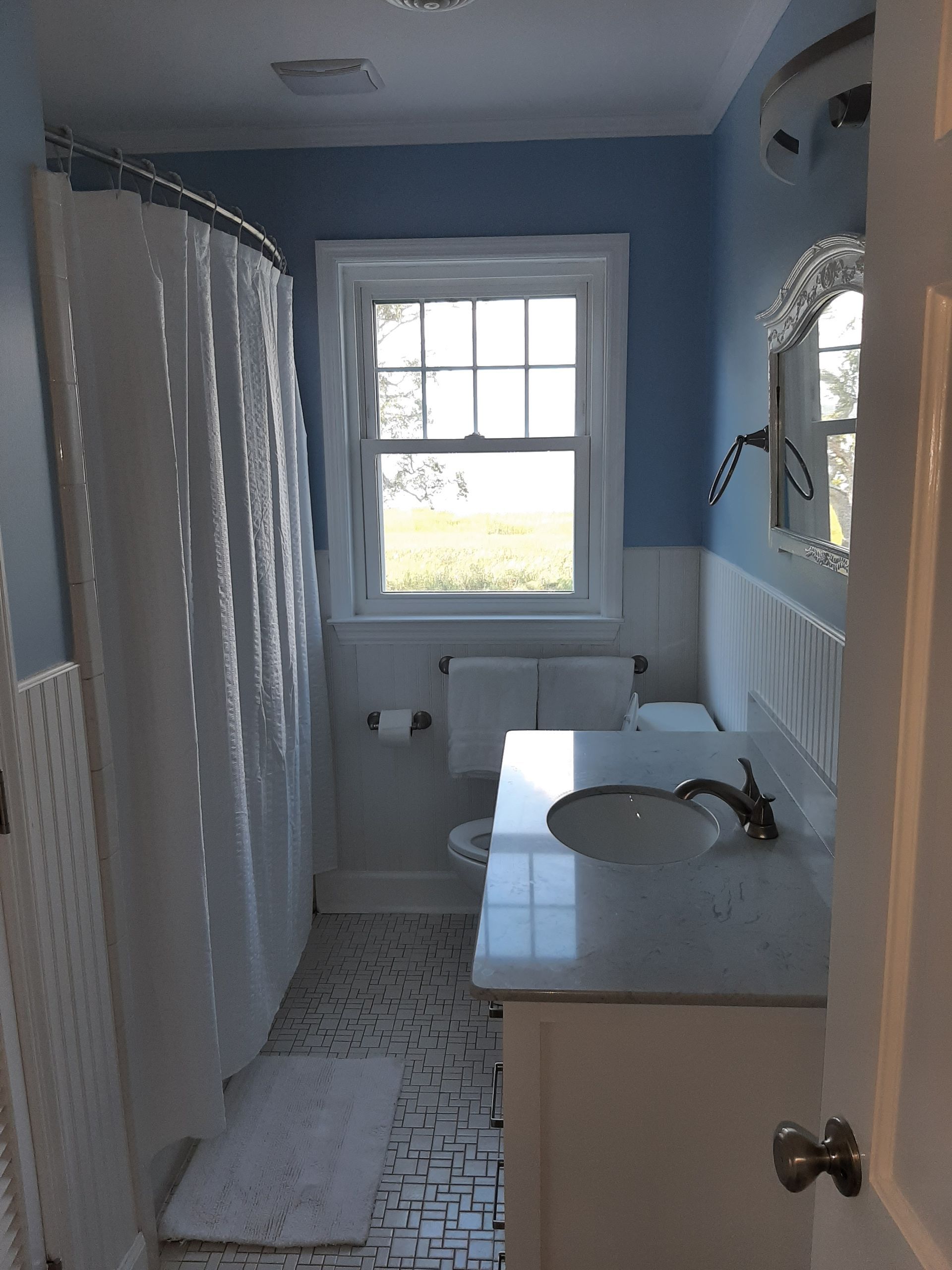 Small blue bathroom with shower curtain, sink, window, and patterned tile floor.