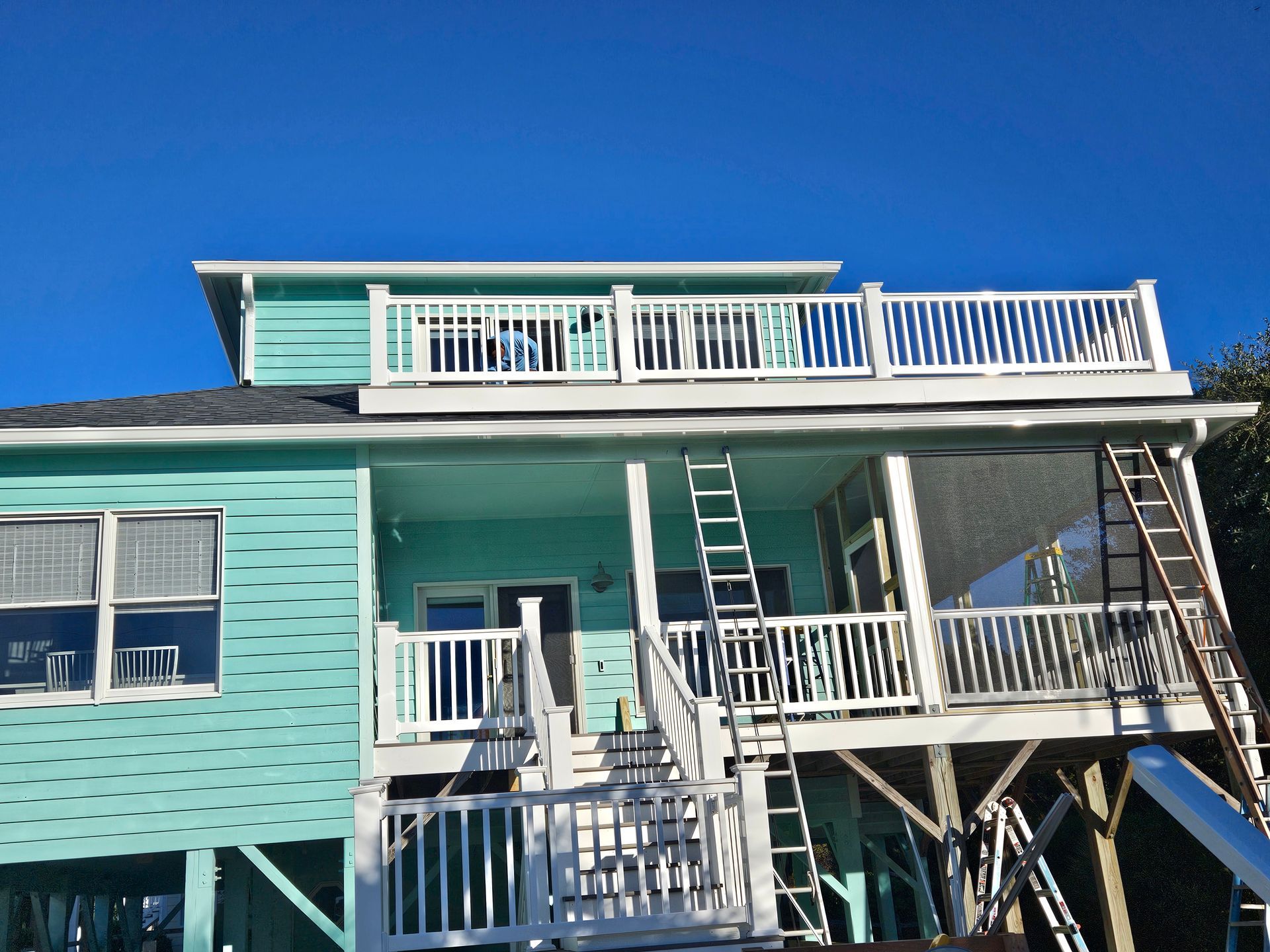 Turquoise beach house with white balconies and stairs under a clear blue sky