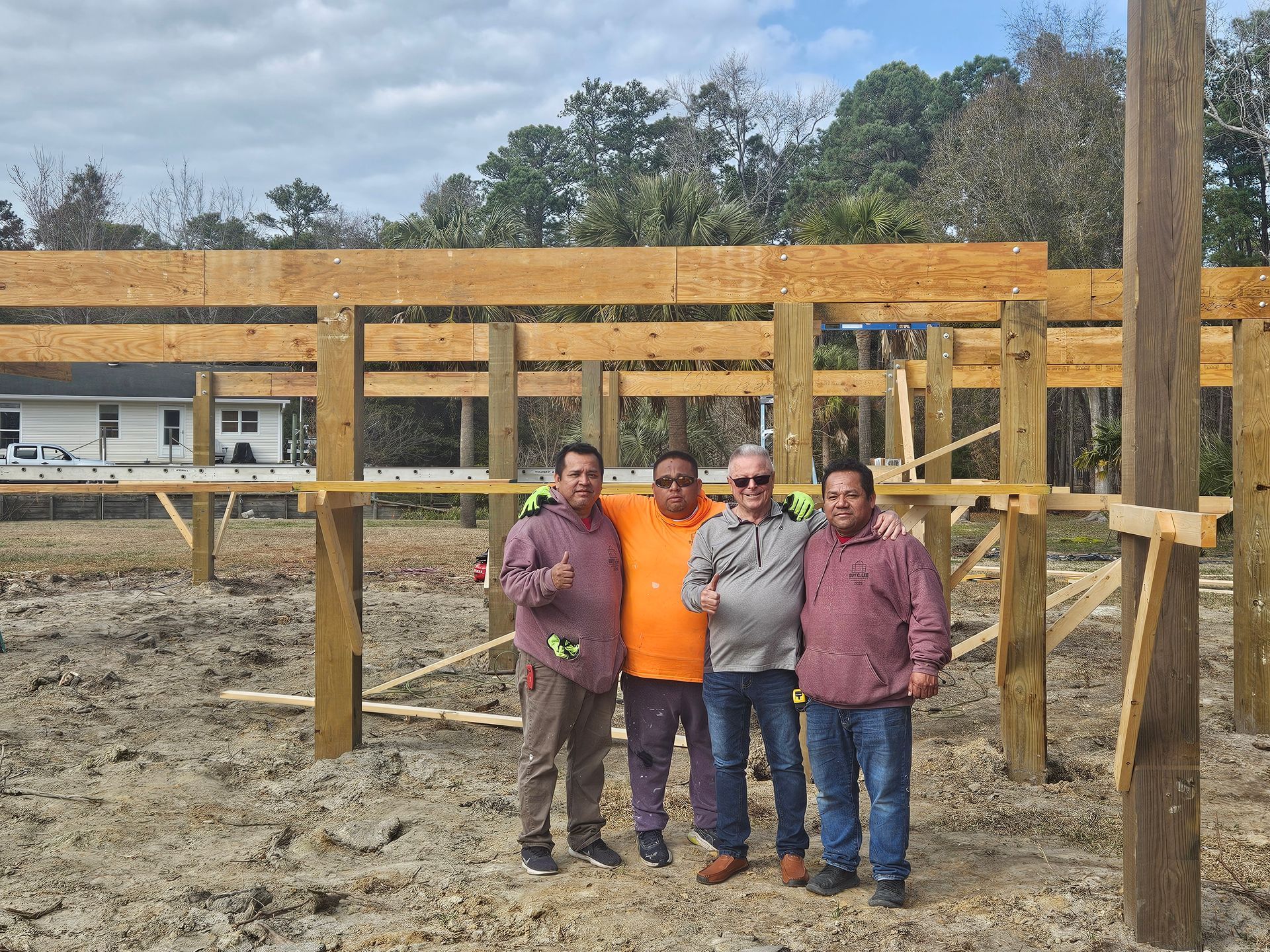 Four people stand in a muddy construction site framed by wooden beams.