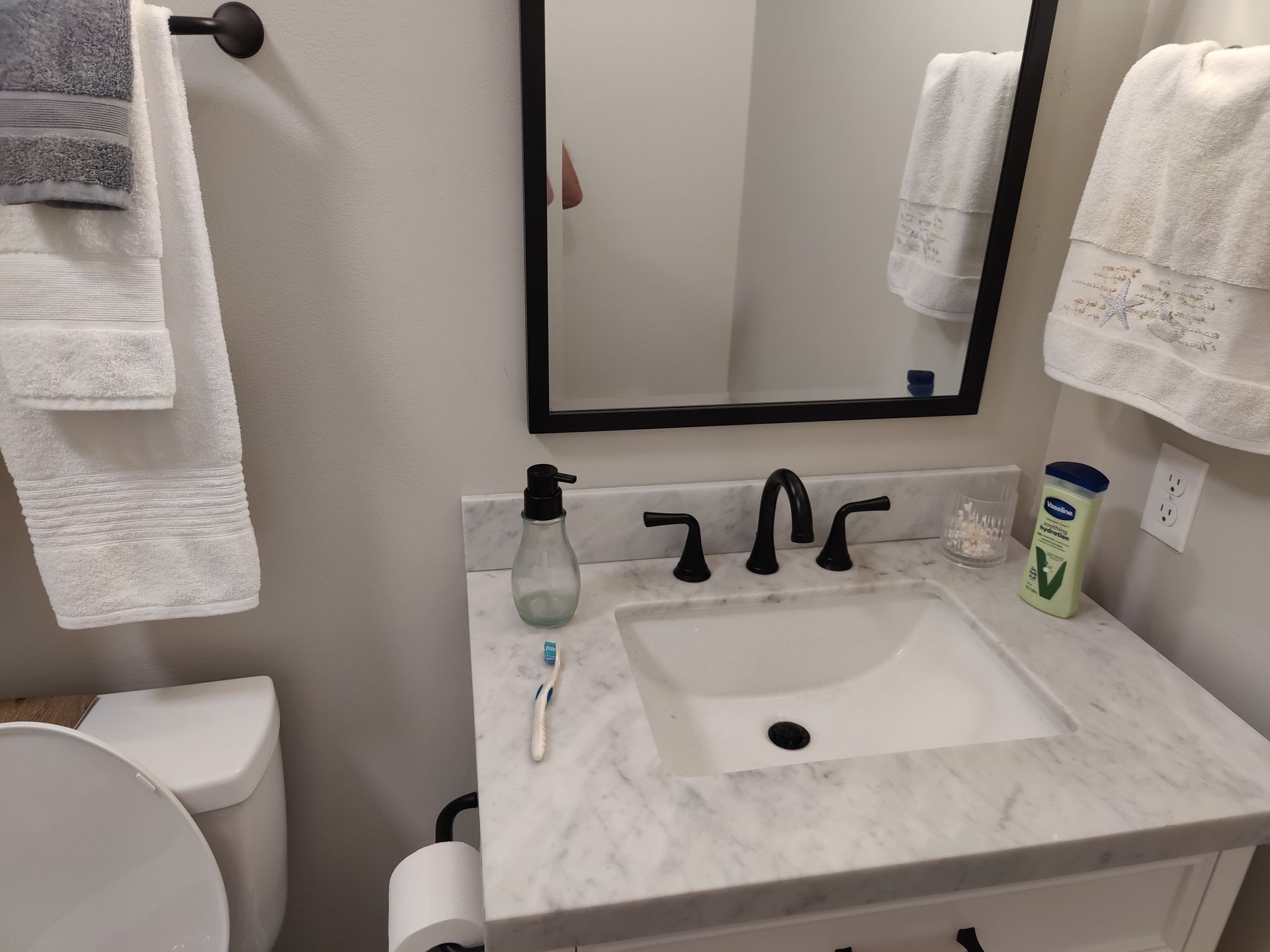 Small bathroom vanity with mirror, white sink, black faucet, soap, toothbrush, and towels.