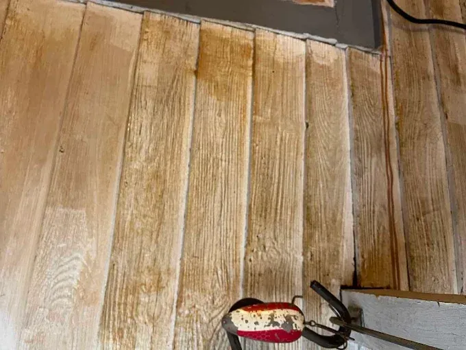 An orbital sander sits on light-colored wood flooring being refinished.