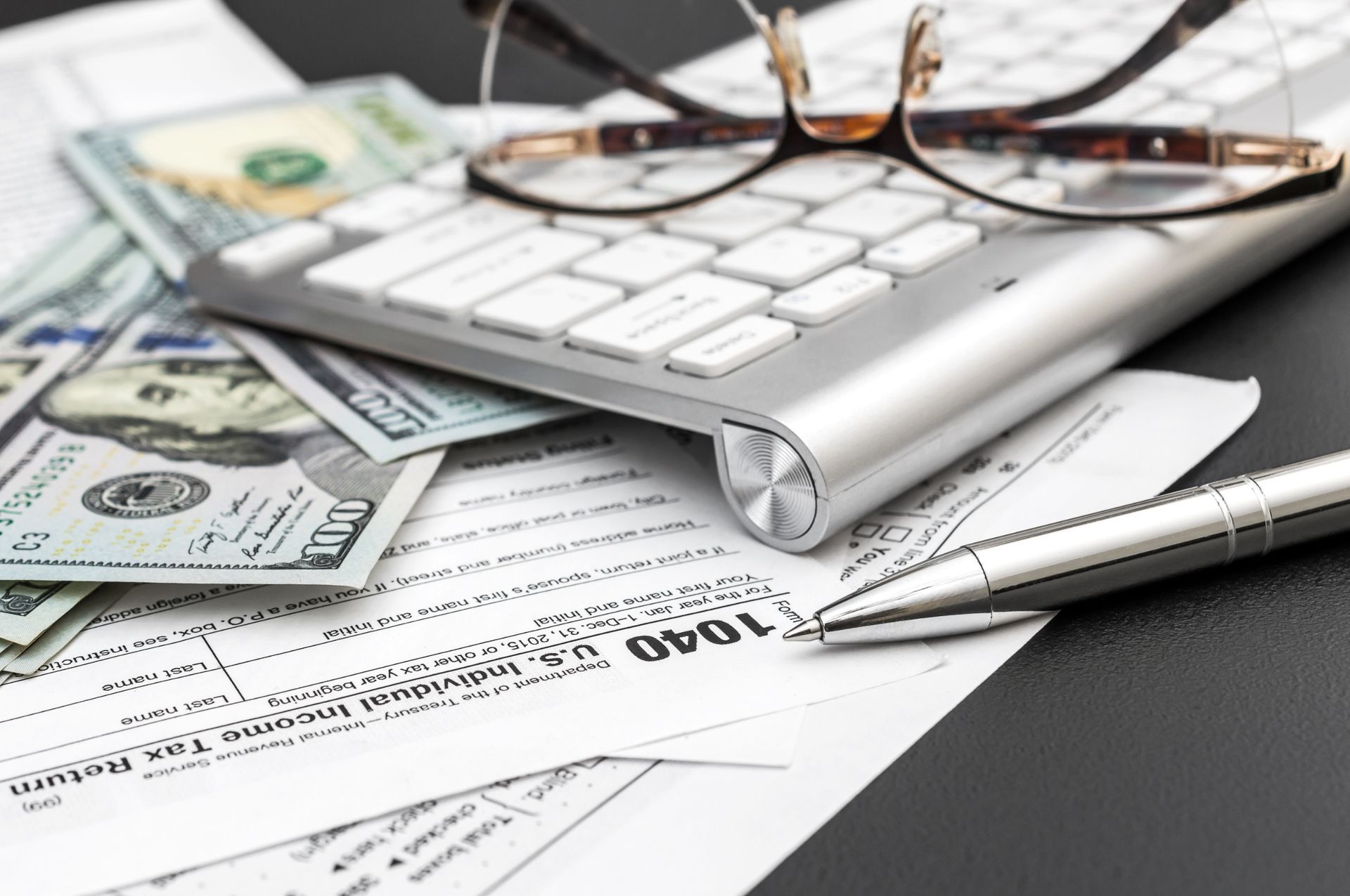 Calculator, eyeglasses, cash, and tax forms on a desk, suggesting financial accounting or budgeting