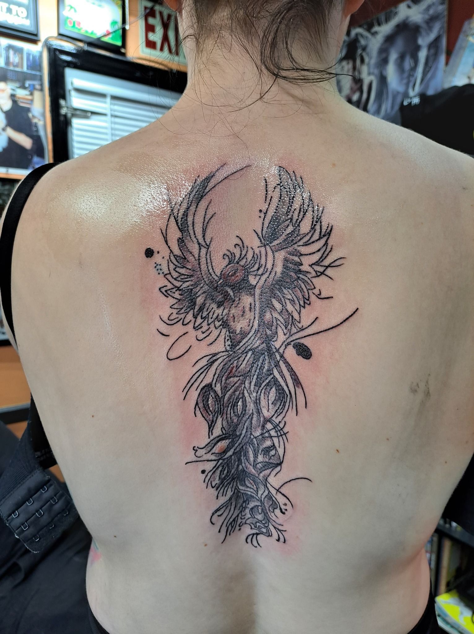 Person's back with a large, abstract black tattoo down the spine, possibly floral. Tattoo is fresh.