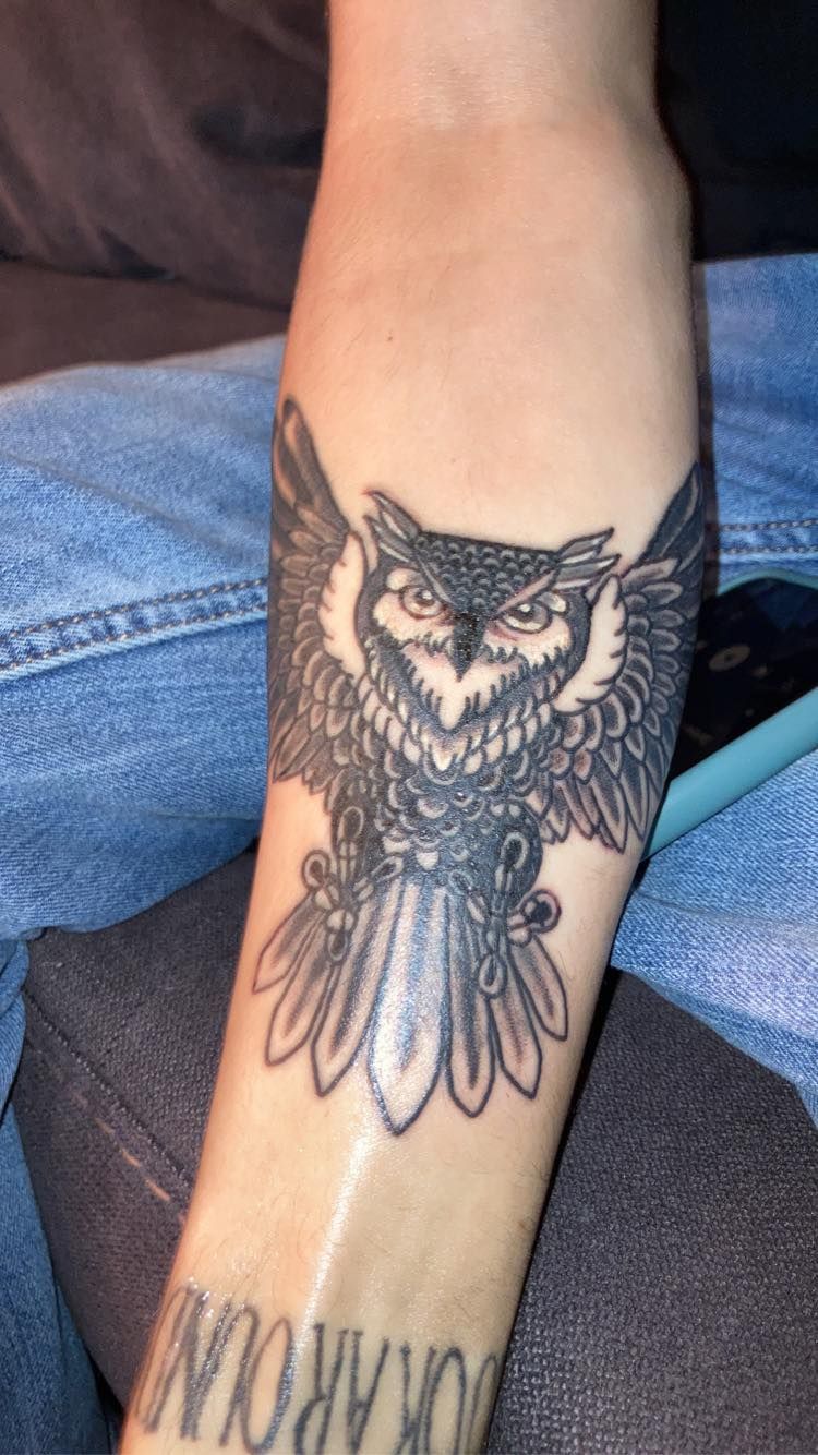 Tattoo of an owl with spread wings on a person's forearm. Black and white detailed design.