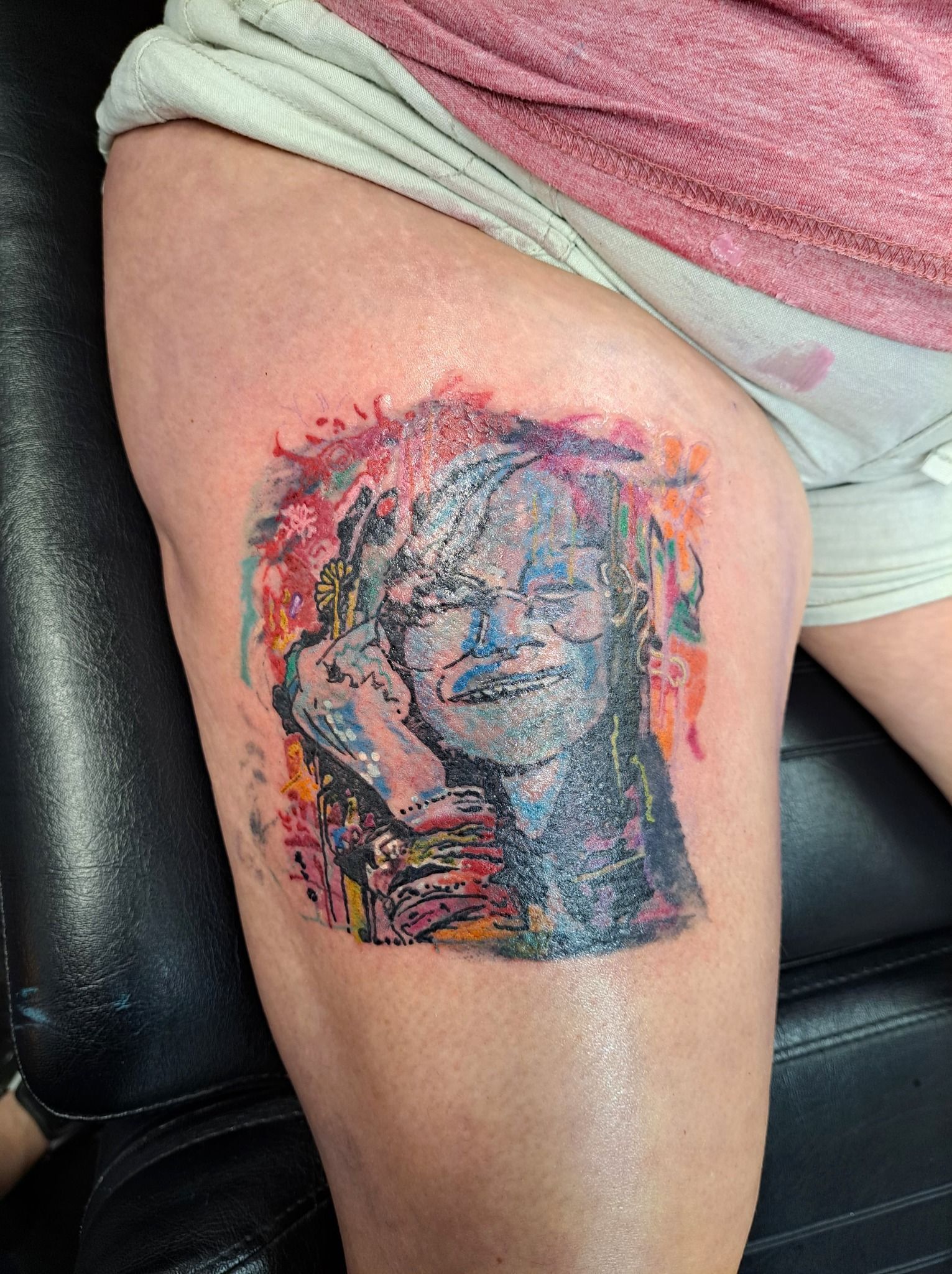 Tattoo of a person's face on a thigh. Colorful abstract background, grayscale face.