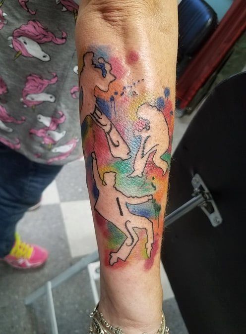 Tattoo of three silhouetted figures on a watercolor background of blues, greens, yellows, and reds on an arm.