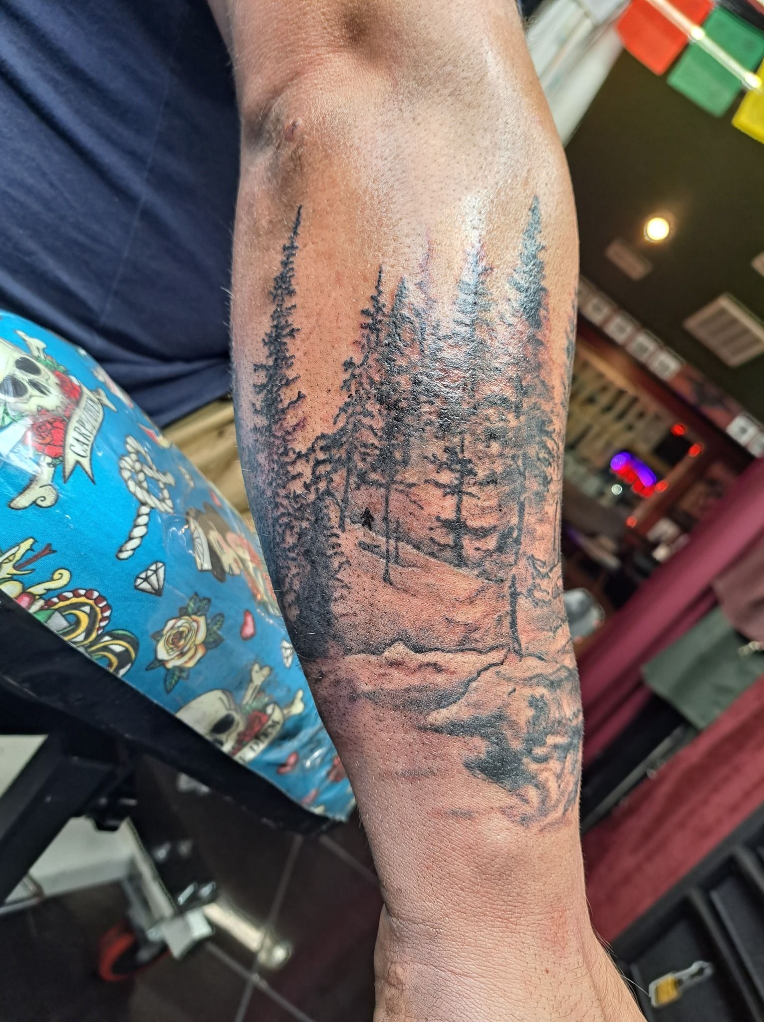 Black ink forest tattoo on an arm, with trees and a small path.