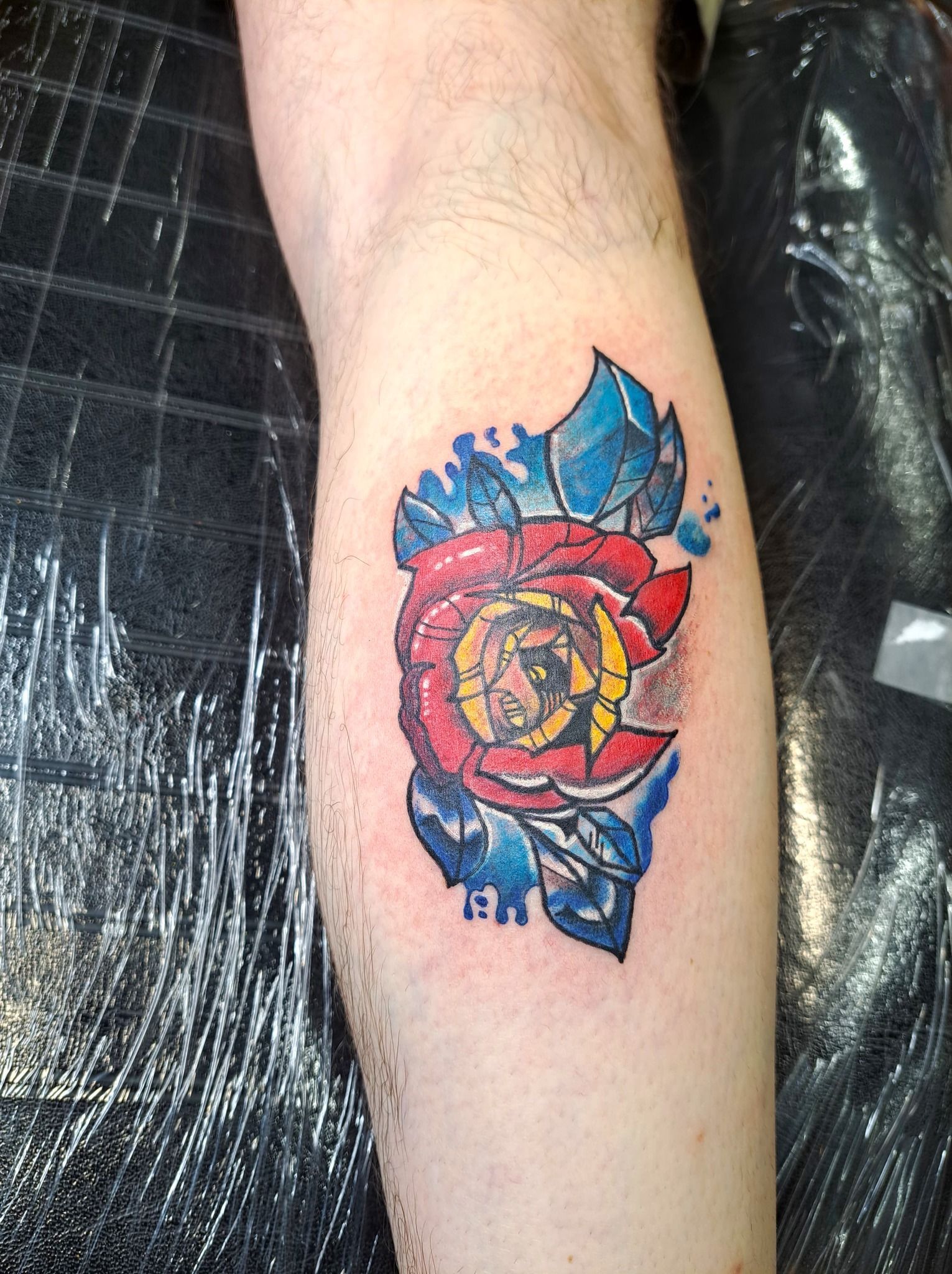 Tattoo of Colorado state flag in the shape of a rose with blue leaves on a person's arm.
