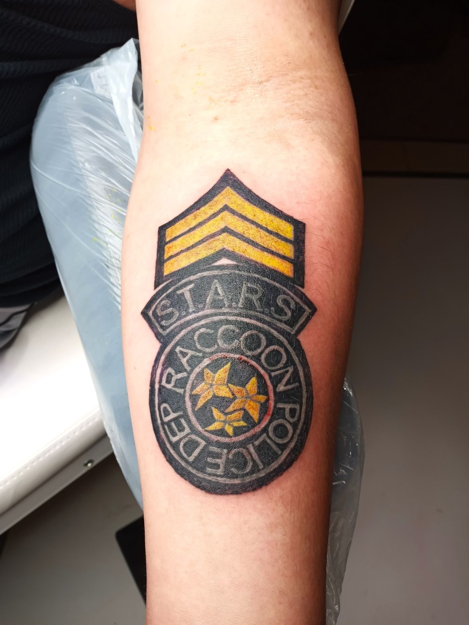 Tattoo of the S.T.A.R.S. badge from Resident Evil on an arm, with yellow and black colors.