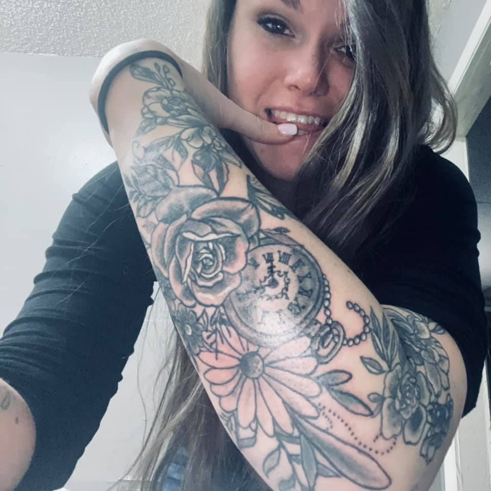 Woman with arm tattoo, biting finger, looking at camera.
