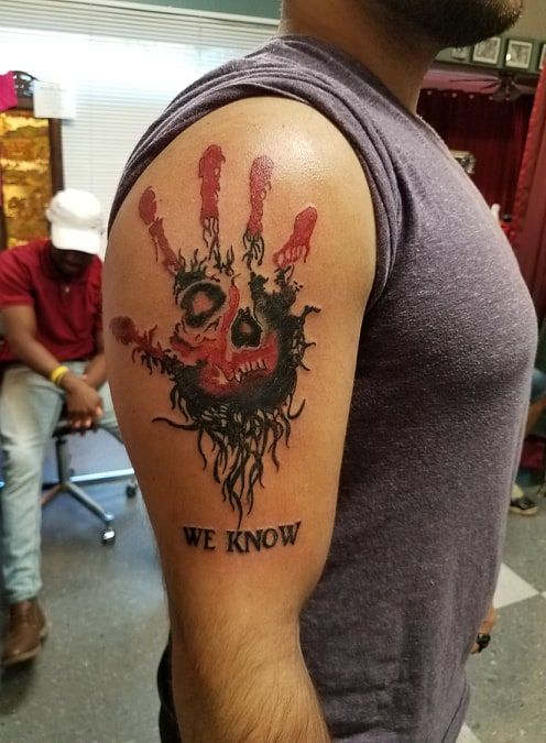 Man's arm with a red skull hand tattoo that says 