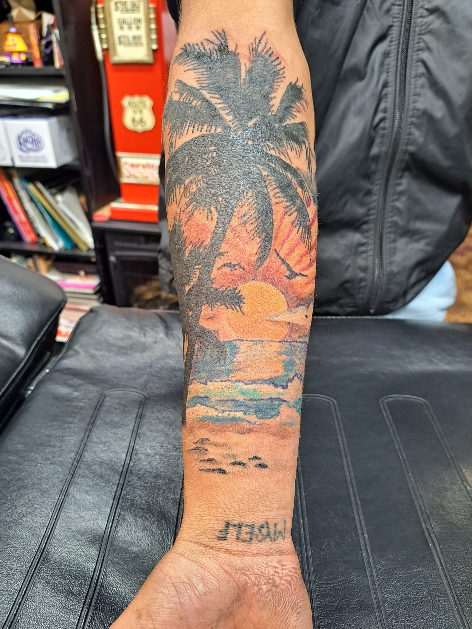 Palm tree and sunset forearm tattoo, with colorful ocean scene.