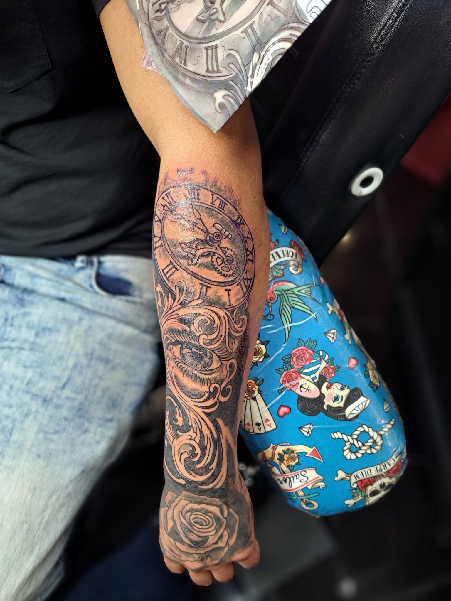 Tattoo of a clock, gears, and flourishes on a forearm, with a rose on the wrist.