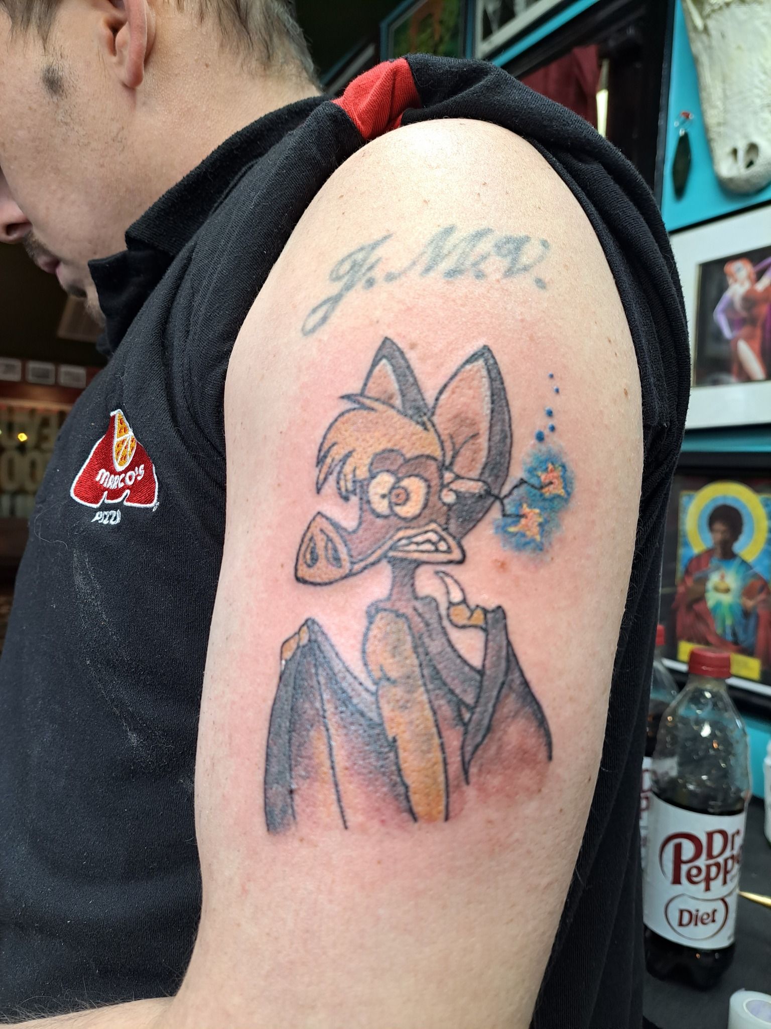 Tattoo of a cartoon bat with a blue aura on a person's arm, with the initials 
