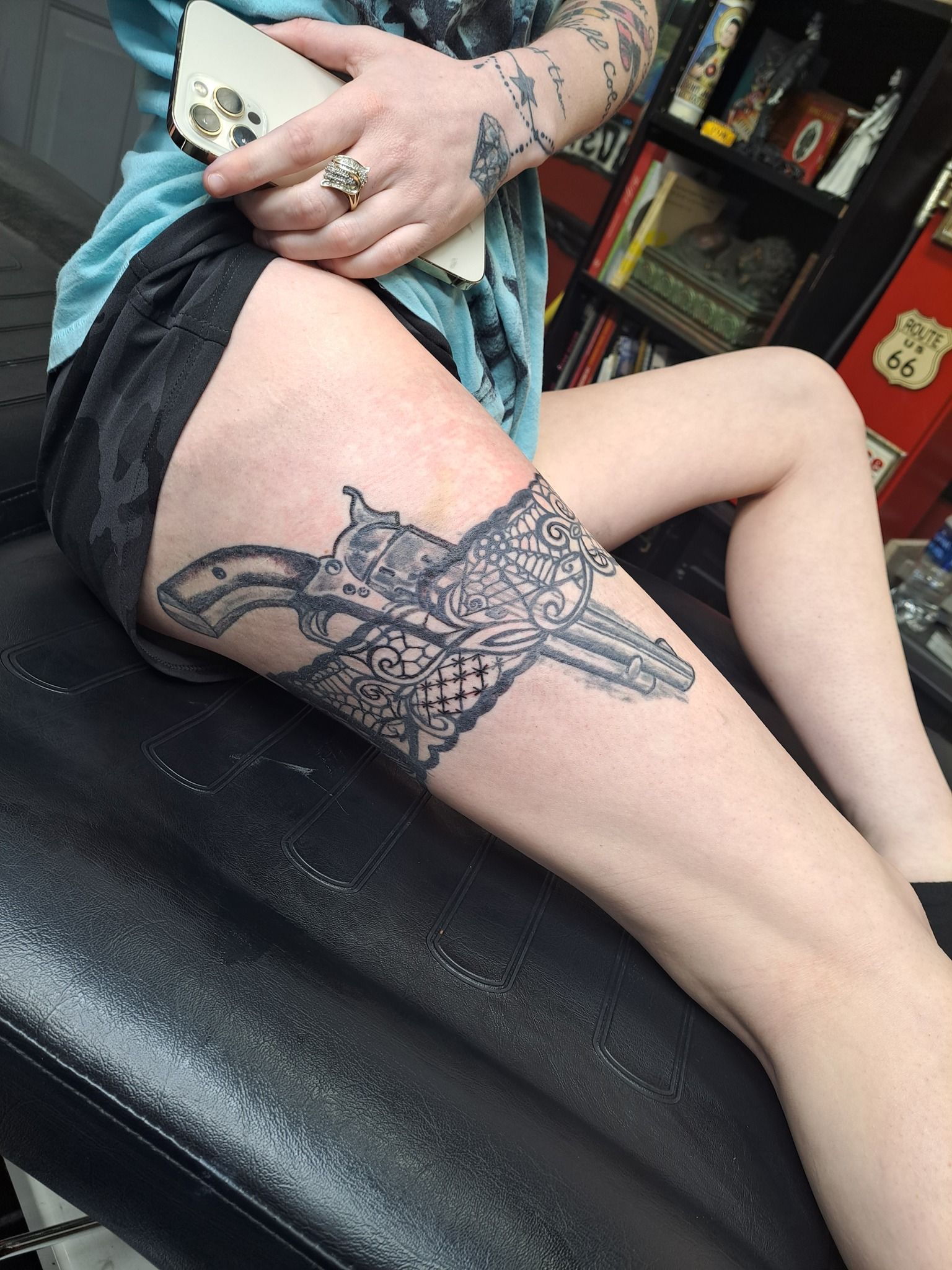 Person with a large tattoo on thigh, holding a phone, sitting on a black chair.