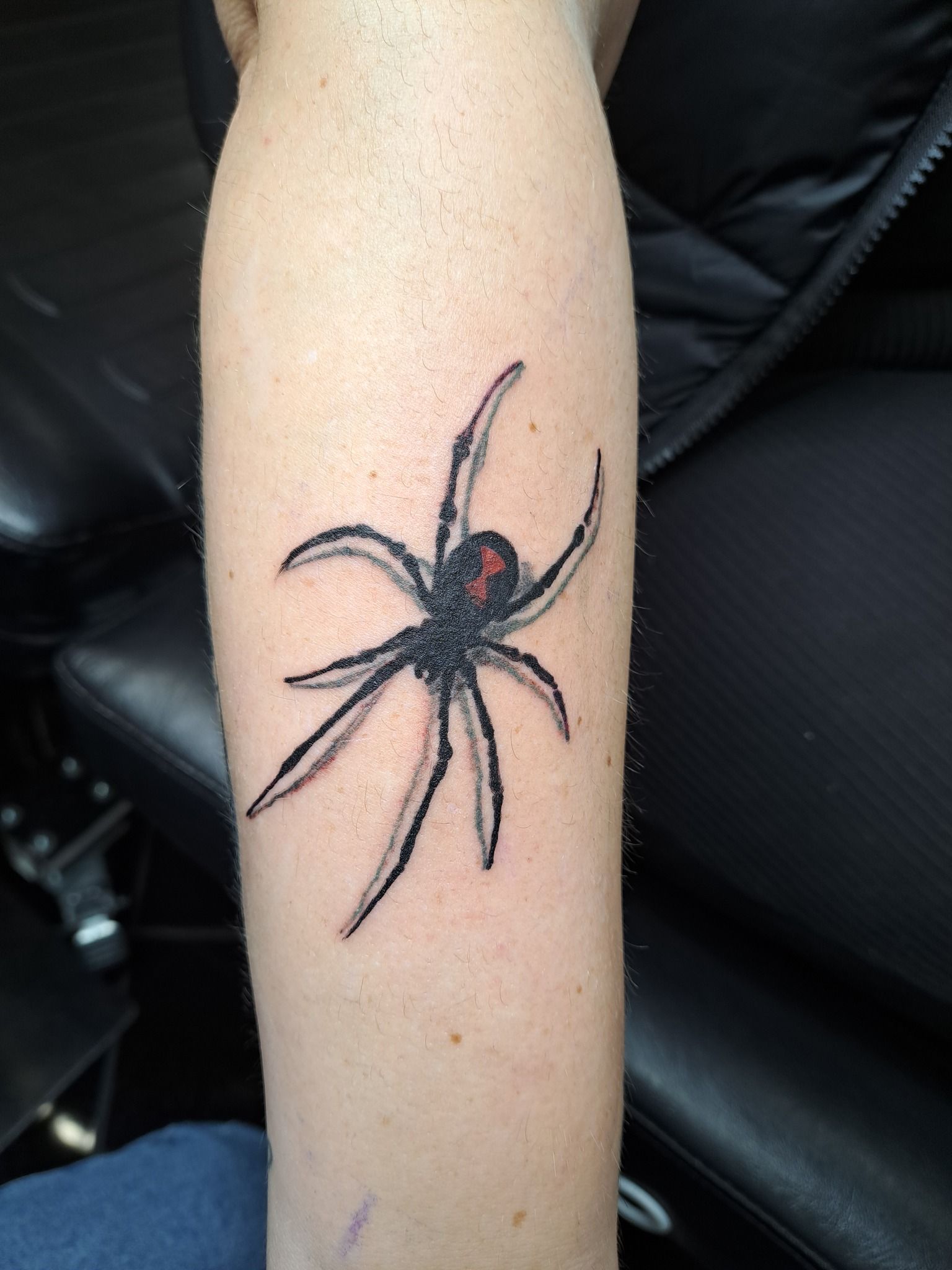 Tattoo of a black spider with a red hourglass on an arm.
