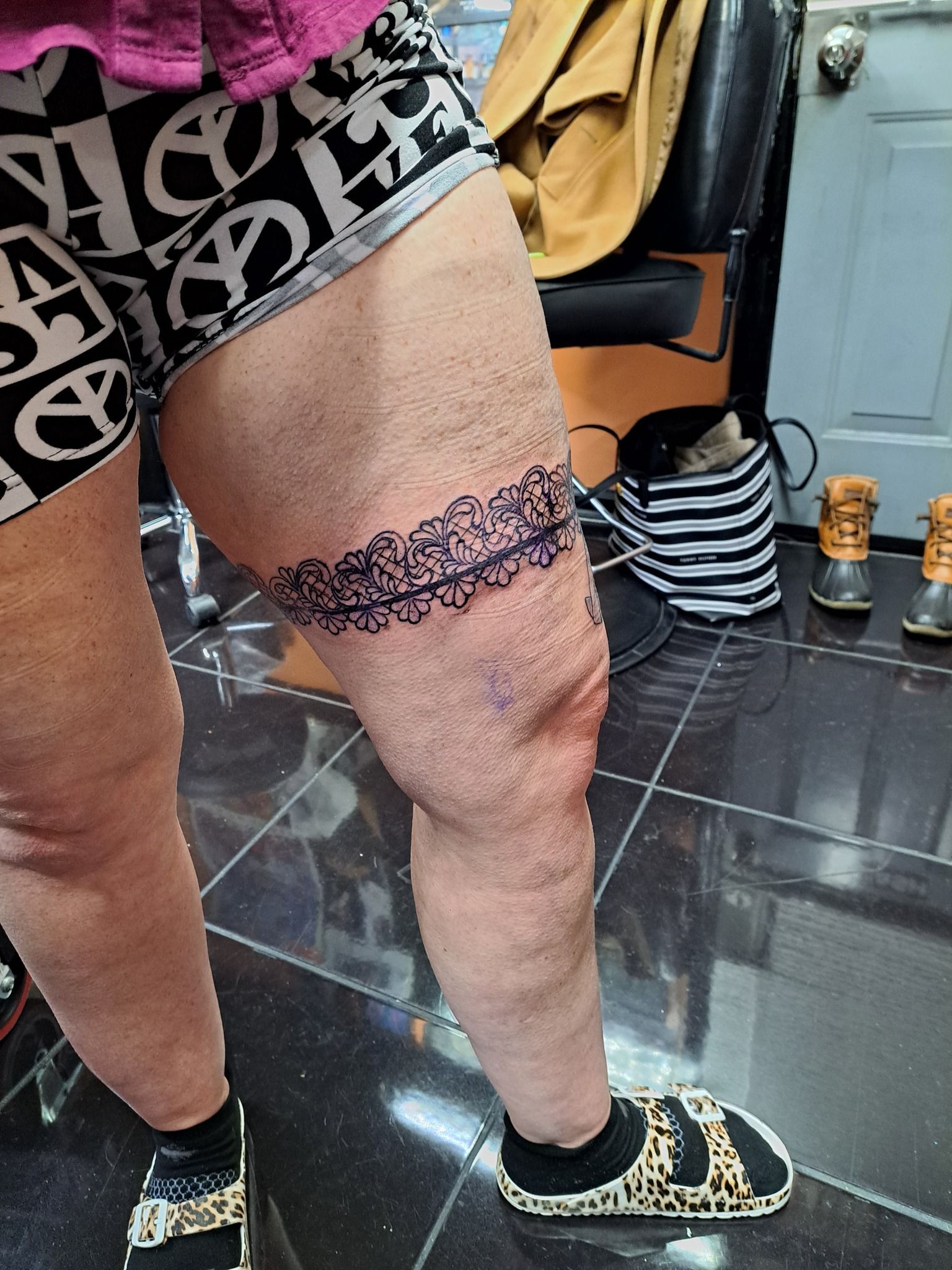 Person's leg with a freshly tattooed garter design above the knee. They wear shorts and sandals.