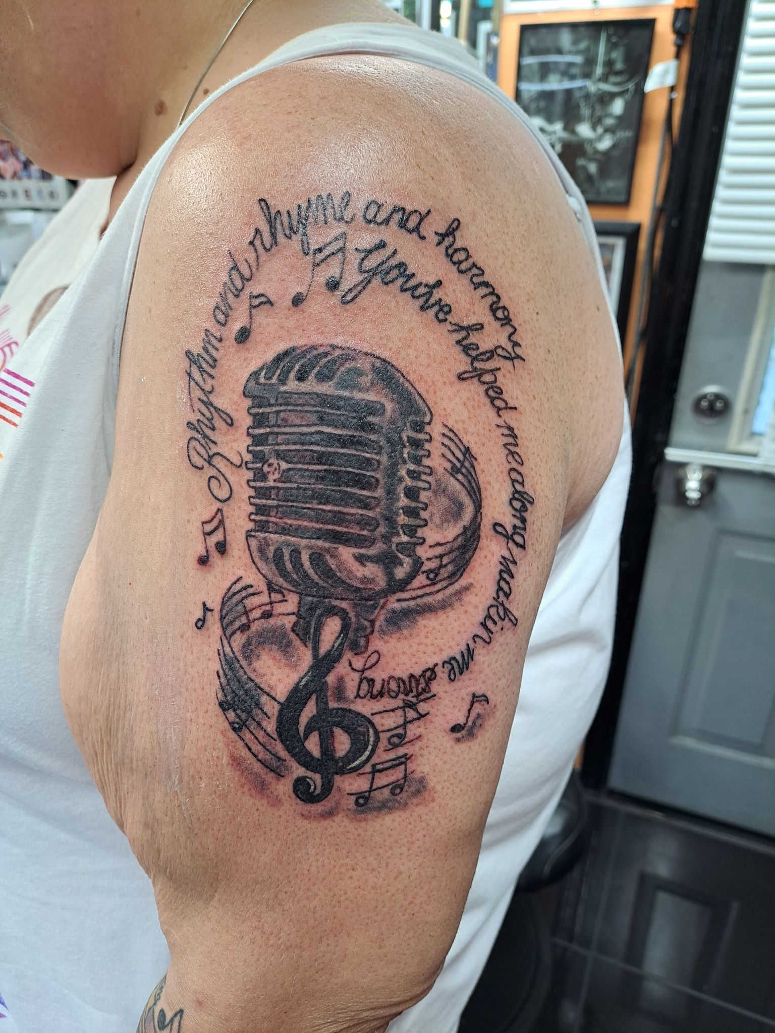 Tattoo of a vintage microphone with music notes and lyrics on a person's upper arm.
