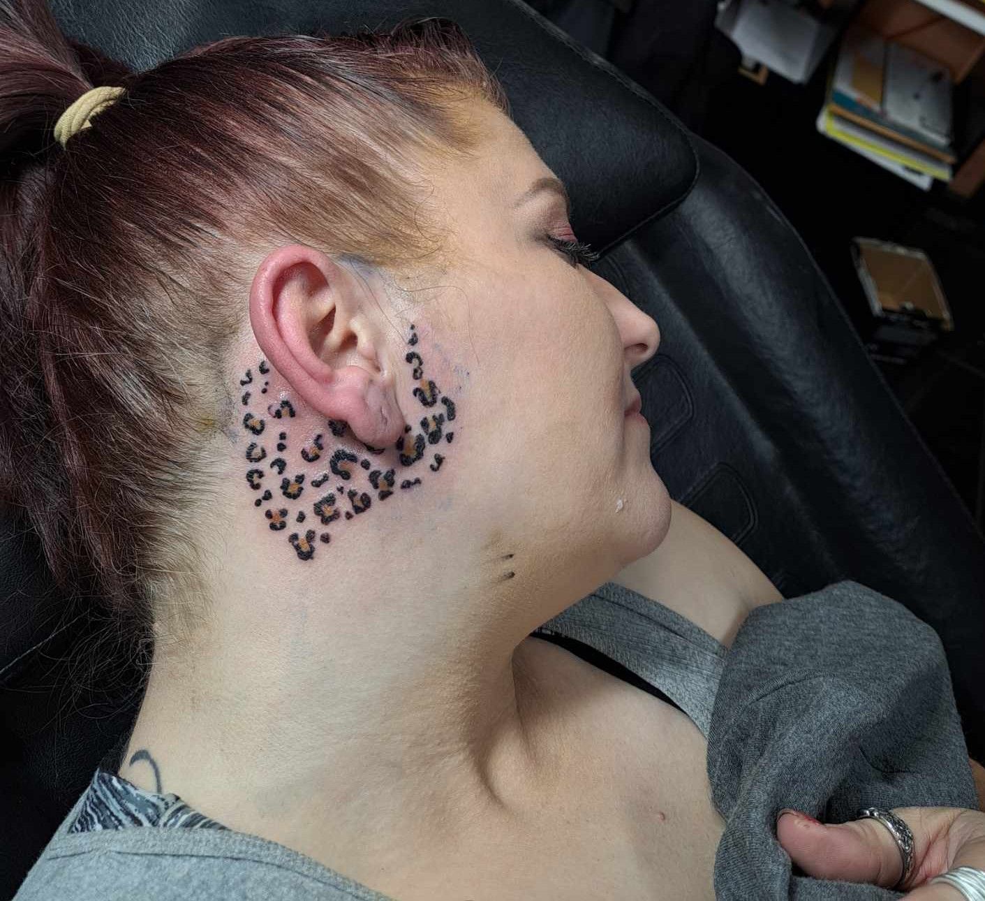 Woman with a neck tattoo of black leopard spots near her ear.