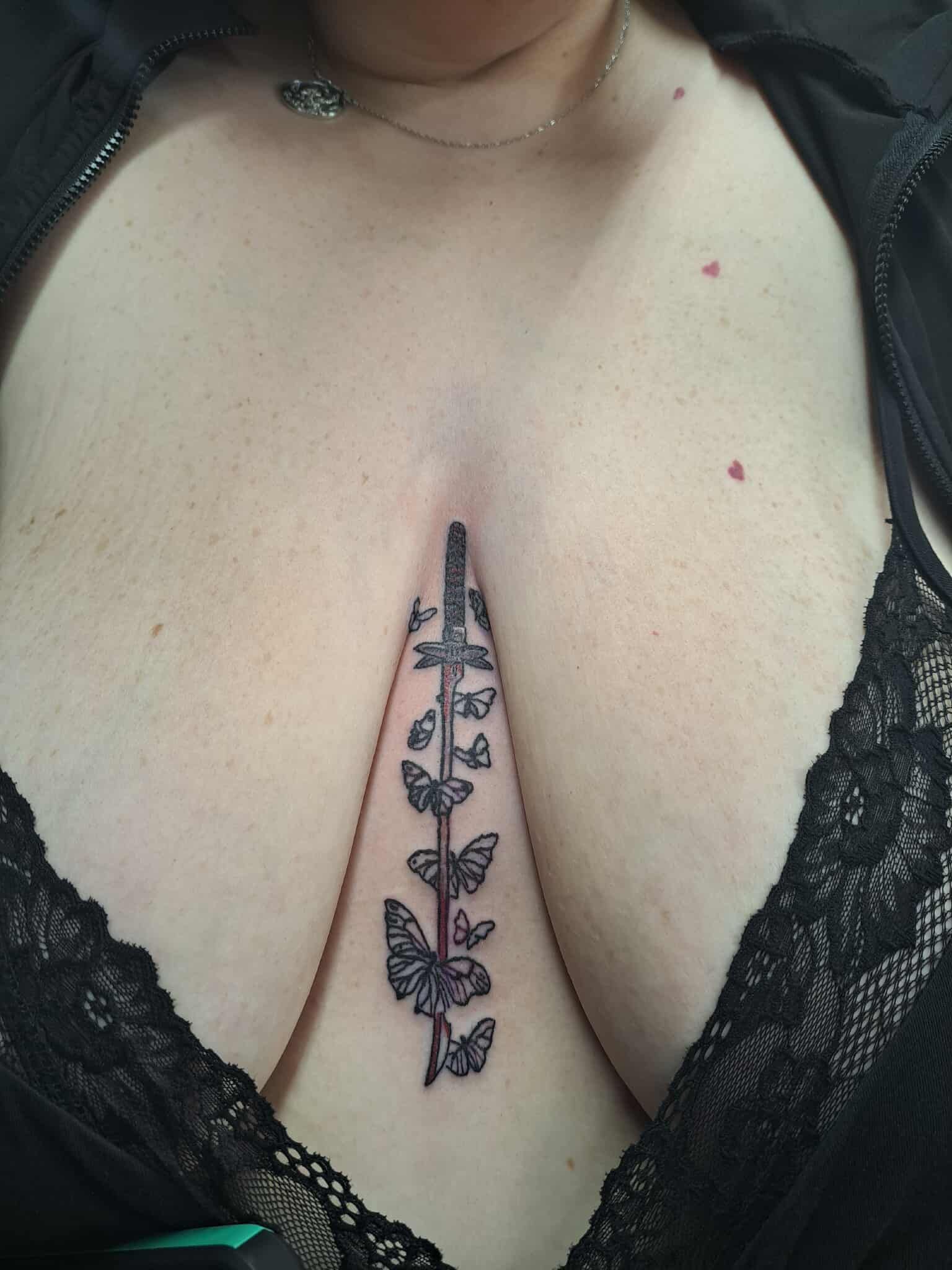 Tattoo of sword and butterflies on a person's chest, visible through low-cut black top.