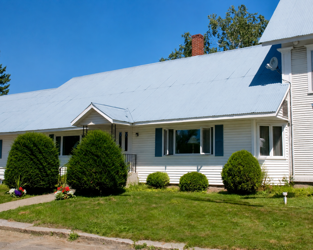 White house with gray roof, trimmed shrubs, and a small front sign under a clear blue sky.