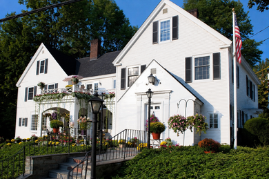 White inn and garden in sunlight with hanging flower baskets and a U.S. flag