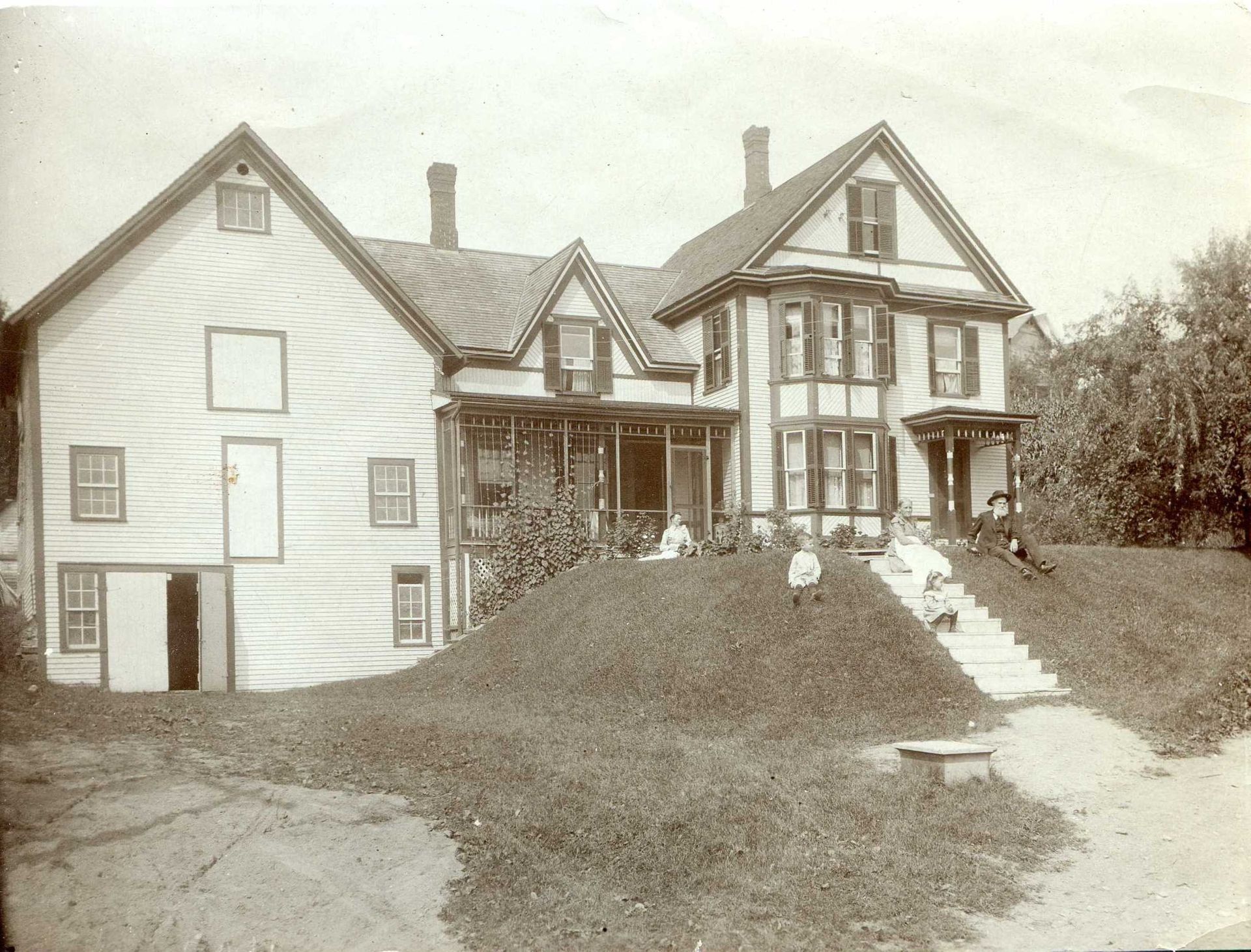 Sepia-toned historic house with front porch, gabled roofs, and stairway up a grassy hill