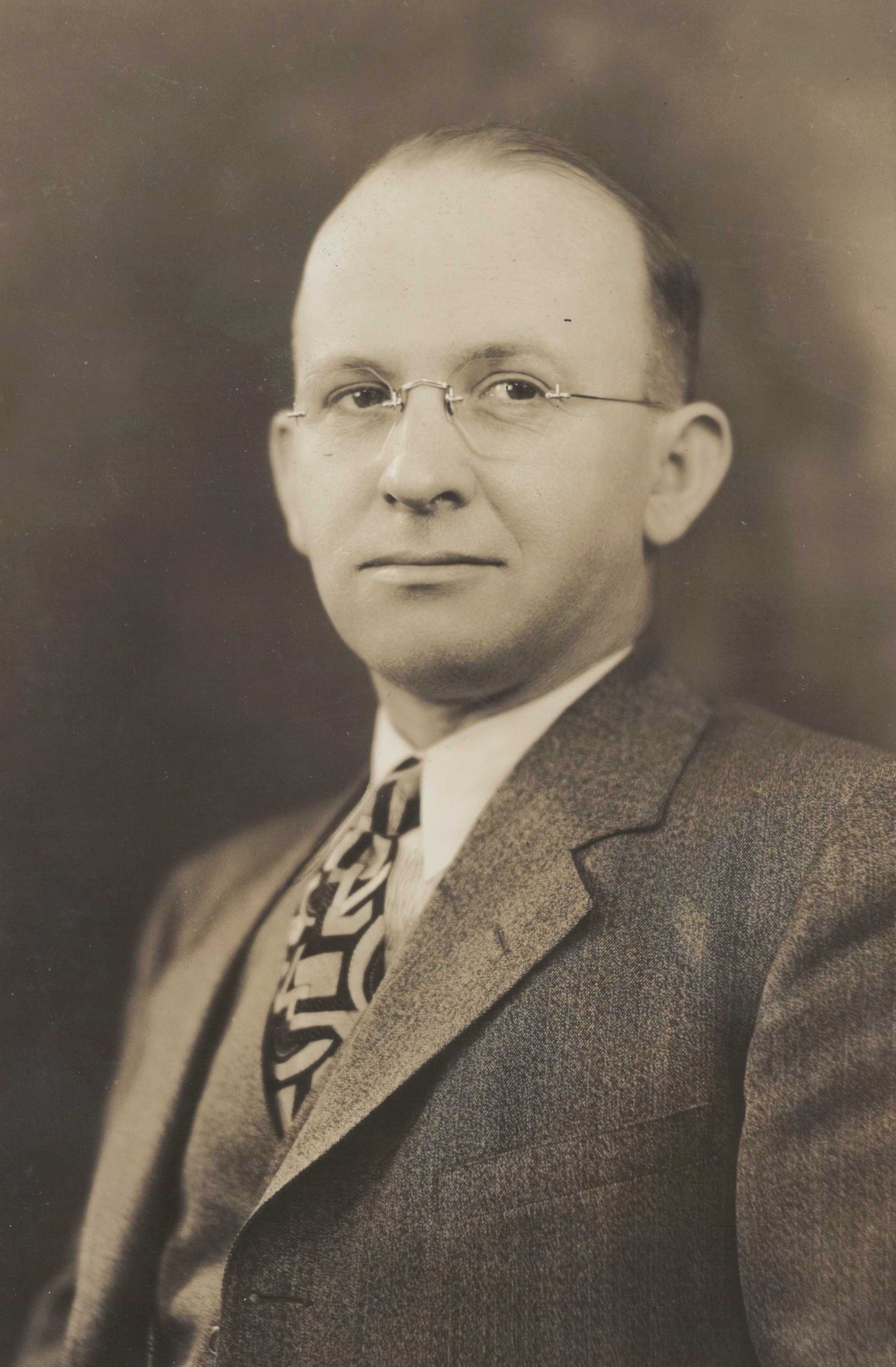 Studio portrait of a man in glasses wearing a suit and patterned tie