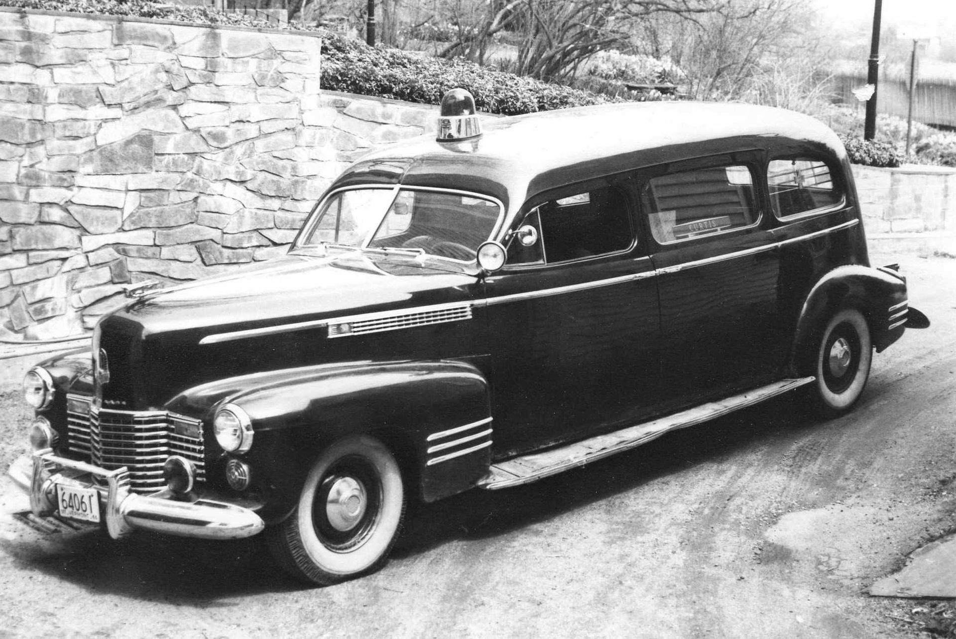 Black vintage sedan parked on a stone-lined road in black and white.