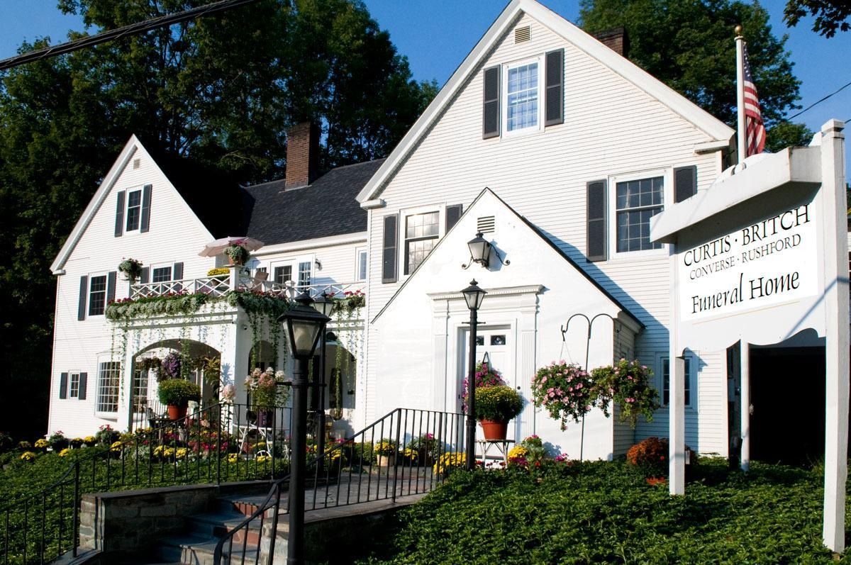 White inn and garden in sunlight with hanging flower baskets and a U.S. flag